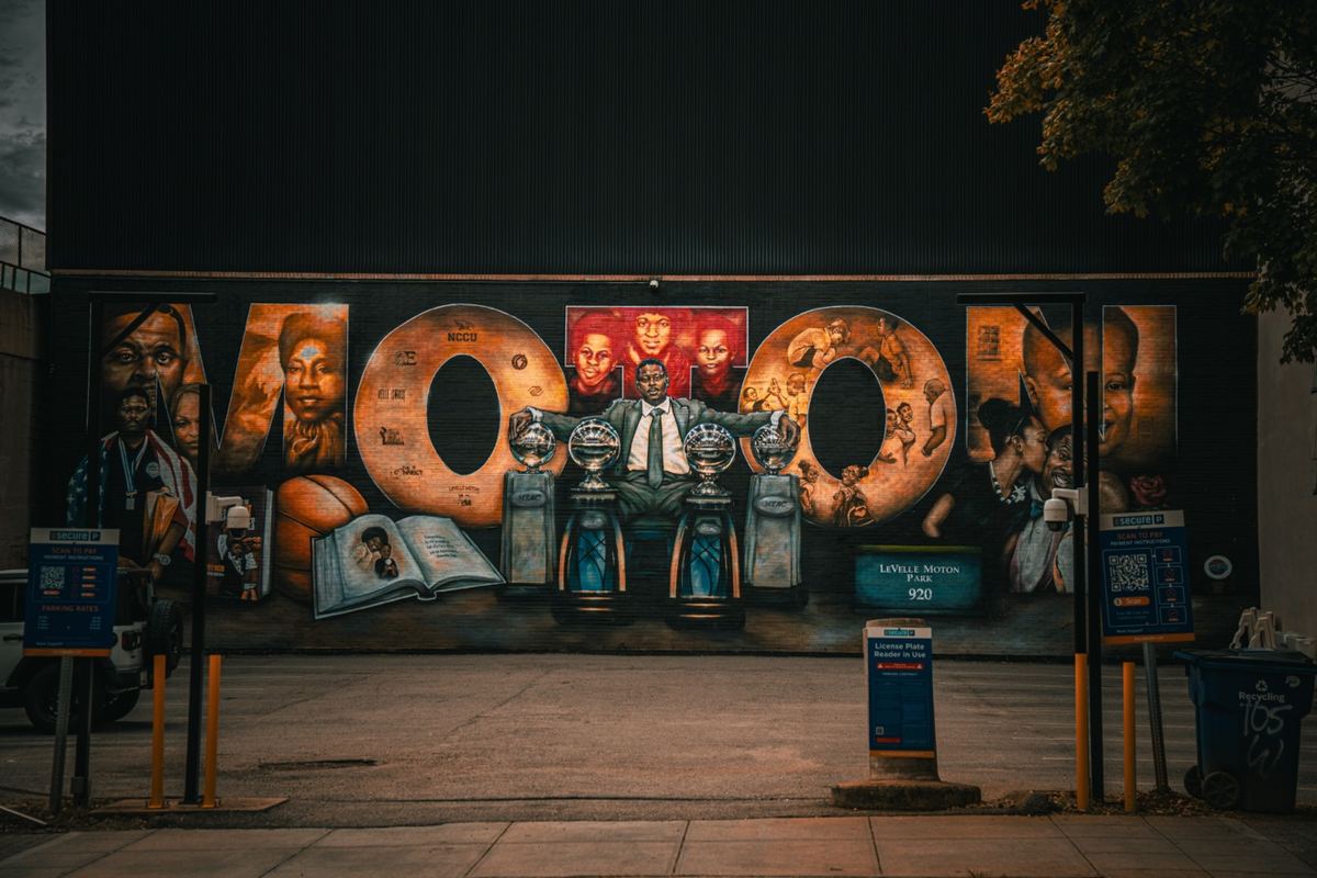 Friends posing in front of a colorful 'Boom' mural on a downtown Raleigh street at night