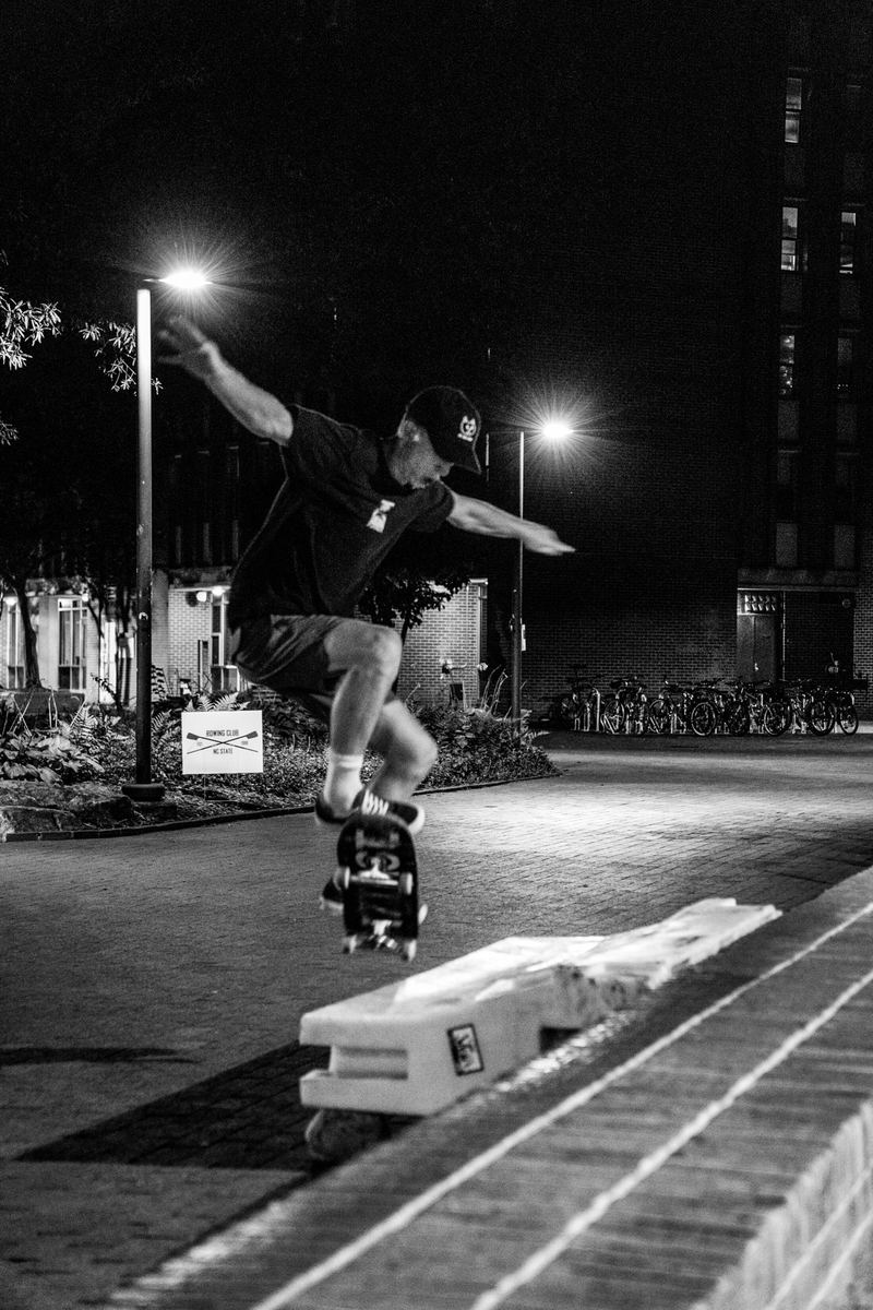 Black-and-white shot of a skateboarder grinding a concrete ledge under streetlights