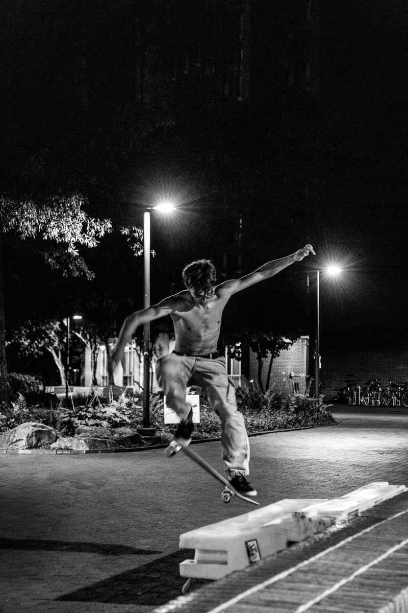 Black-and-white photo of a shirtless skateboarder riding at night under streetlights in Raleigh