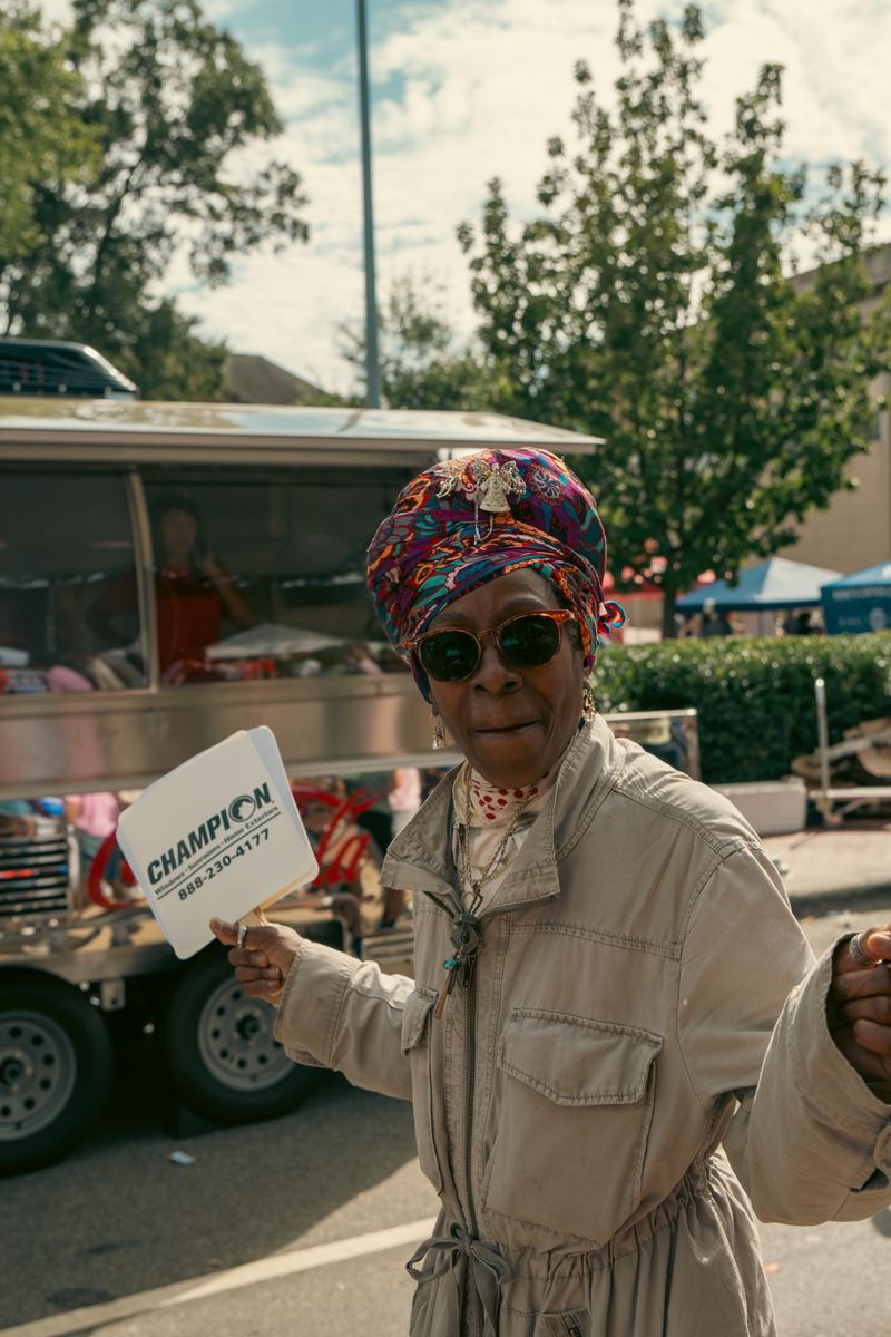 Smiling woman in a colorful headwrap holding a 'Champion' sign at a Raleigh street festival