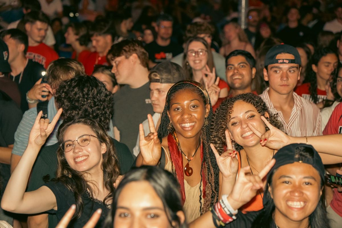 Concert crowd flashing peace signs at a nighttime outdoor show in Raleigh