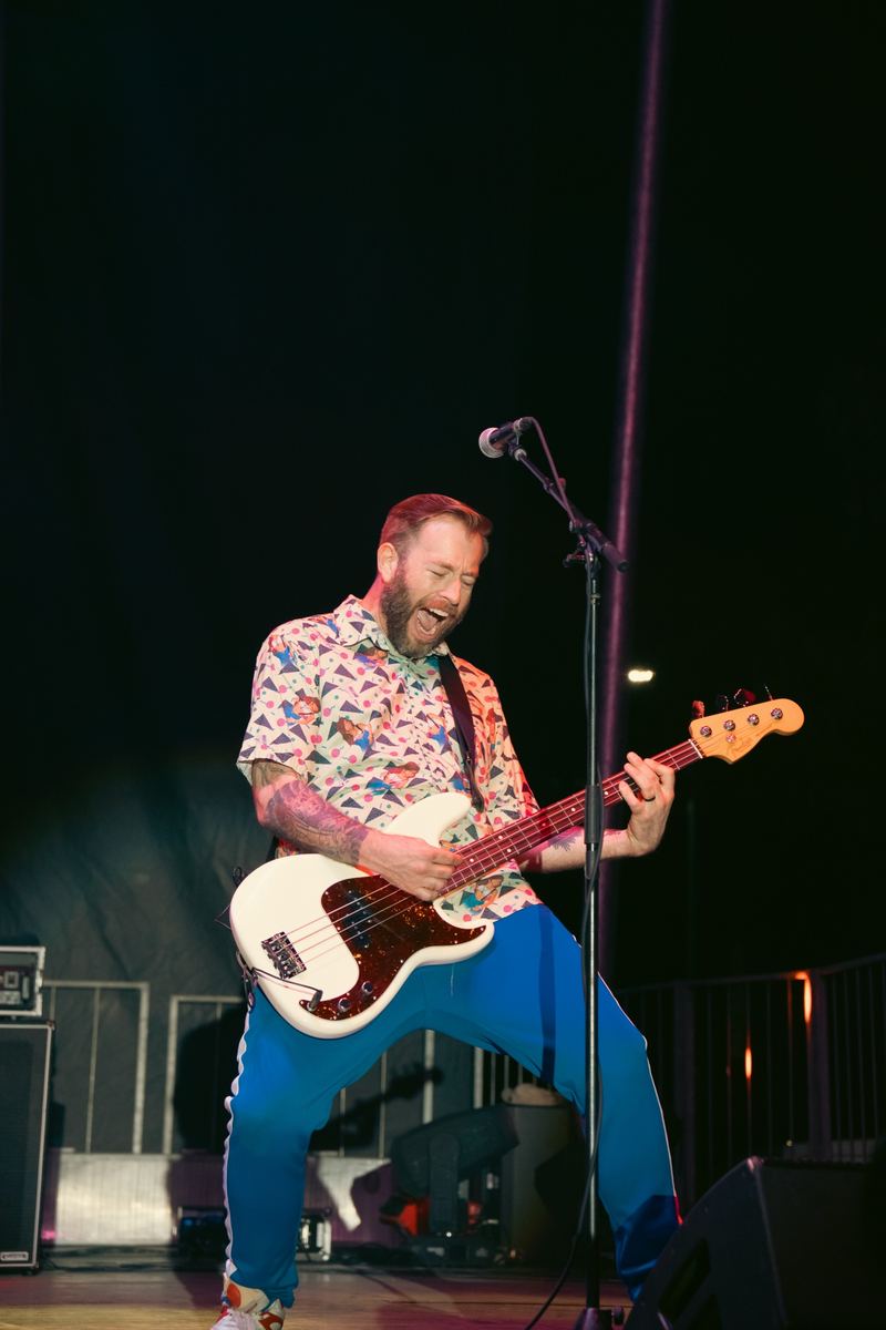 Bassist performing on stage at a nighttime outdoor concert in Raleigh