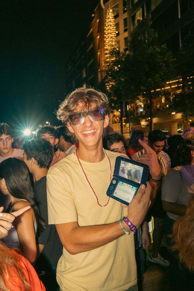 Smiling concertgoer holding up a digital camera in a nighttime crowd in Raleigh
