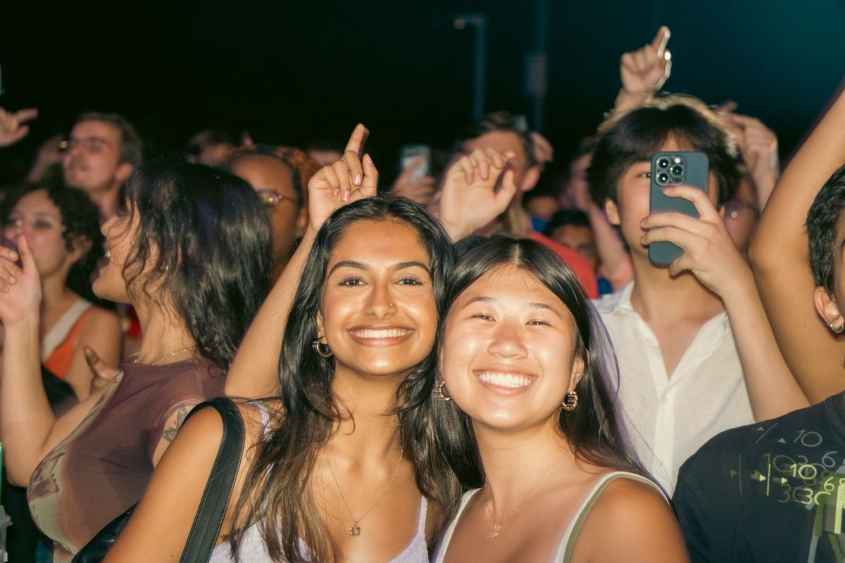 Two young women smiling in a concert crowd at night in Raleigh