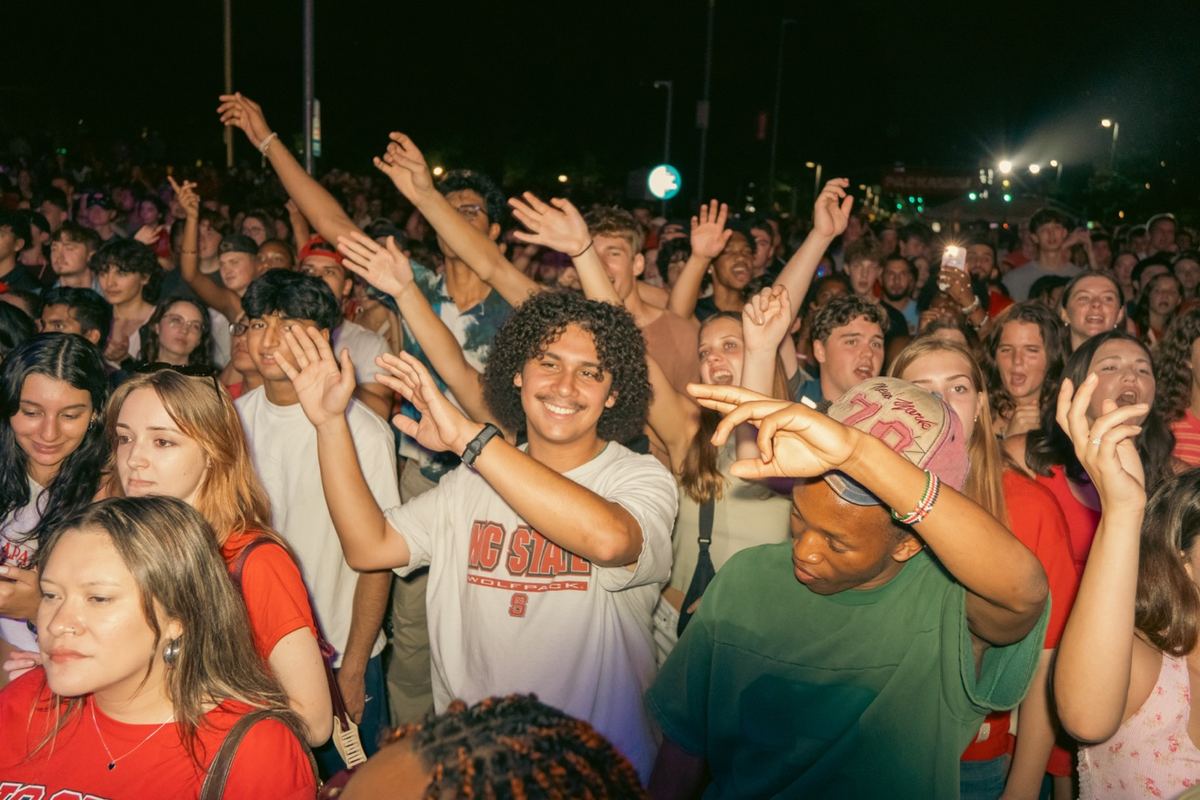 Concert crowd with hands in the air at a nighttime outdoor show in Raleigh