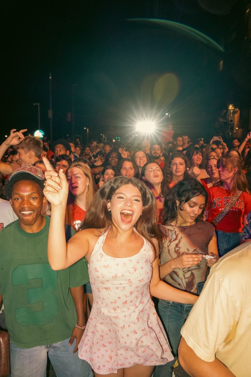 Young woman cheering with her hand raised in a nighttime concert crowd in Raleigh