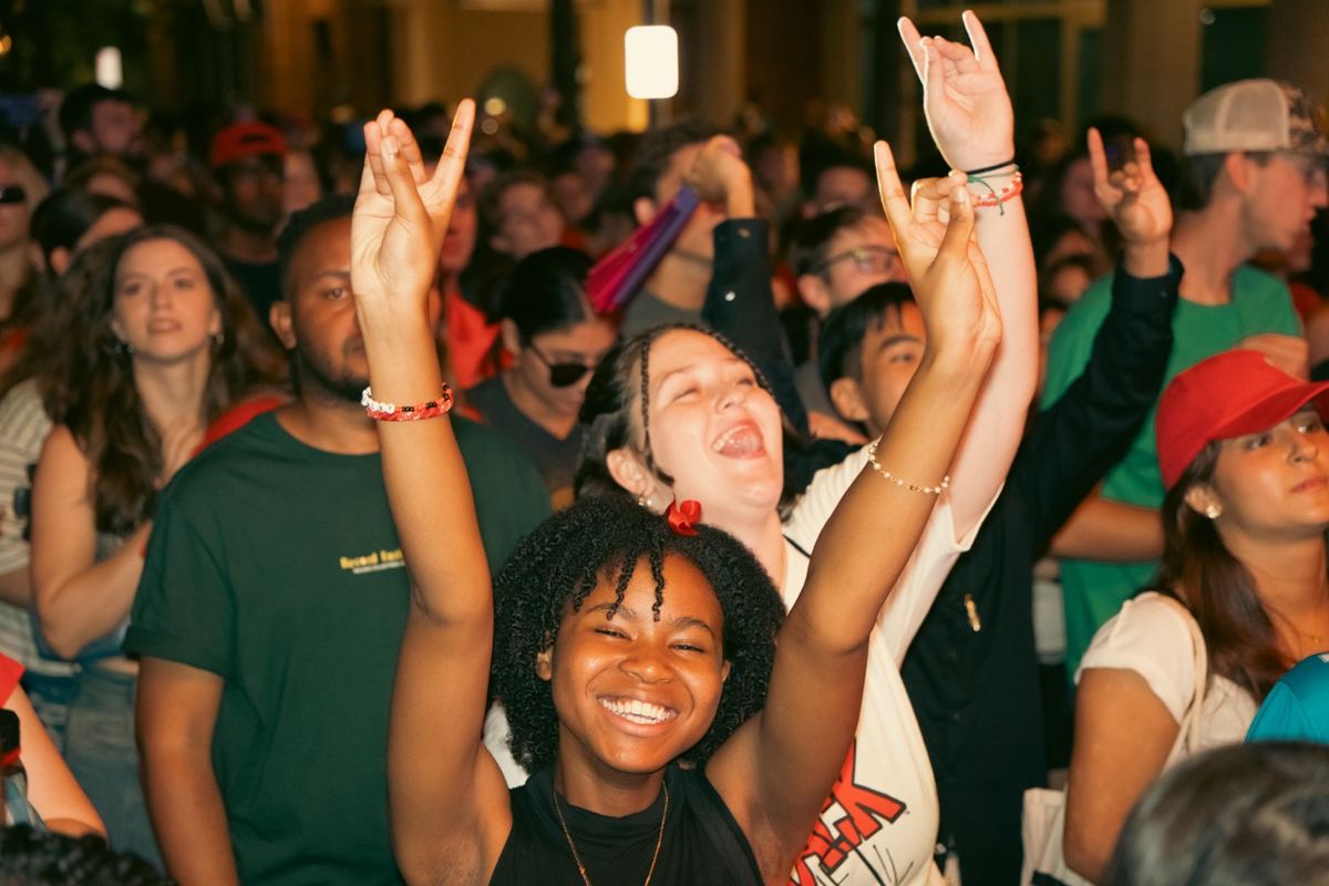 Friends cheering with arms raised at a nighttime outdoor concert in Raleigh