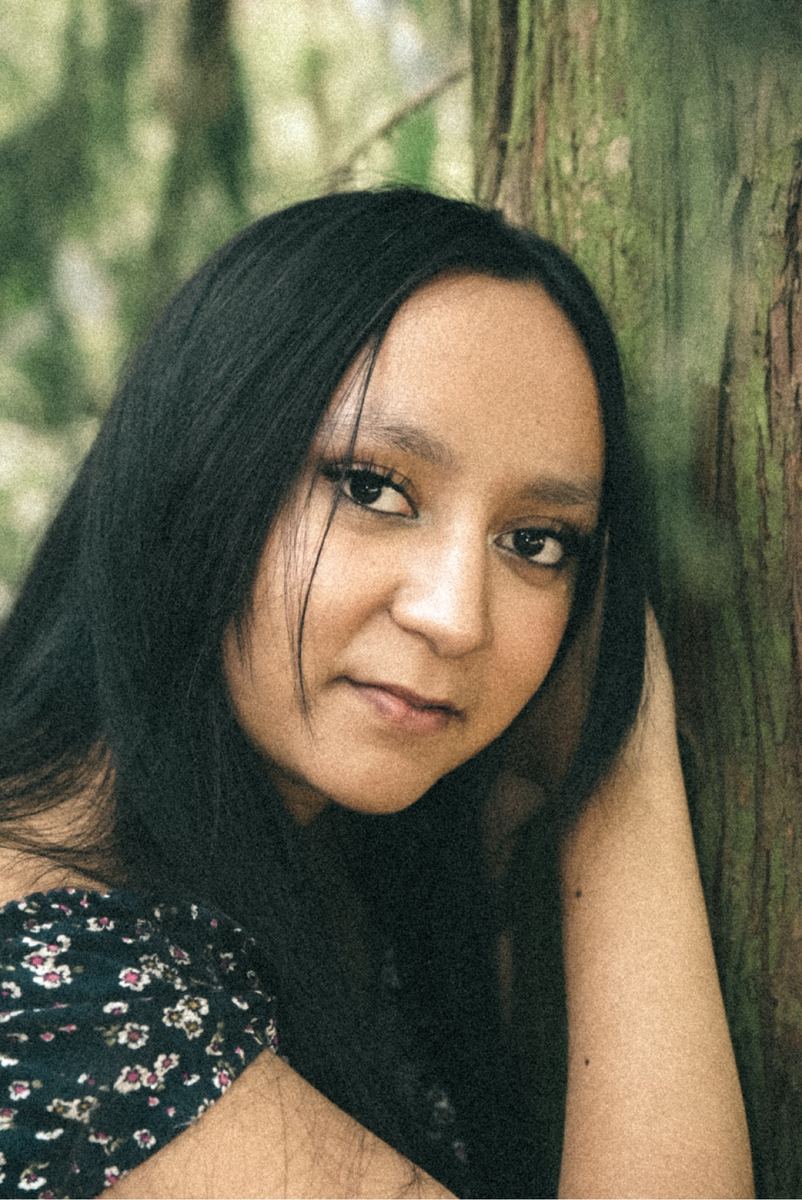 Moody outdoor portrait of a young woman leaning against a tree trunk in Raleigh