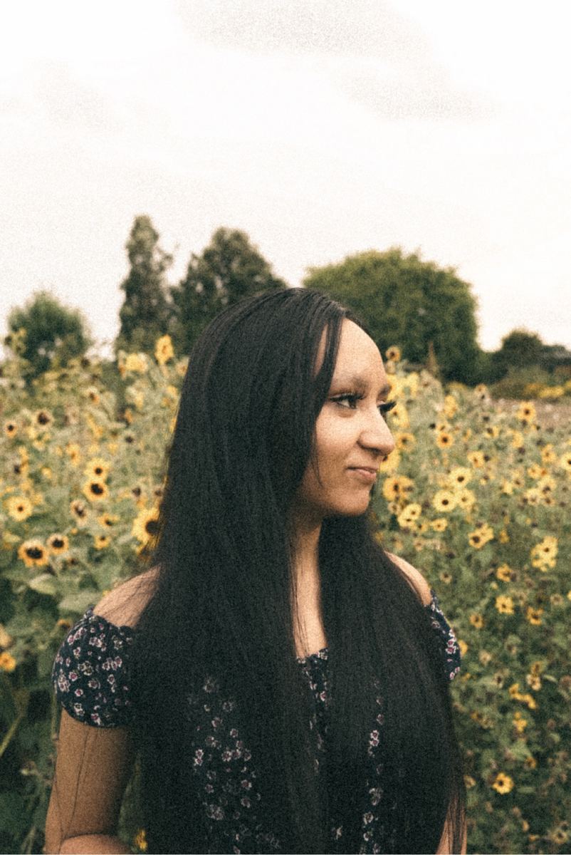 Profile portrait of a young woman in a blooming sunflower field at golden hour