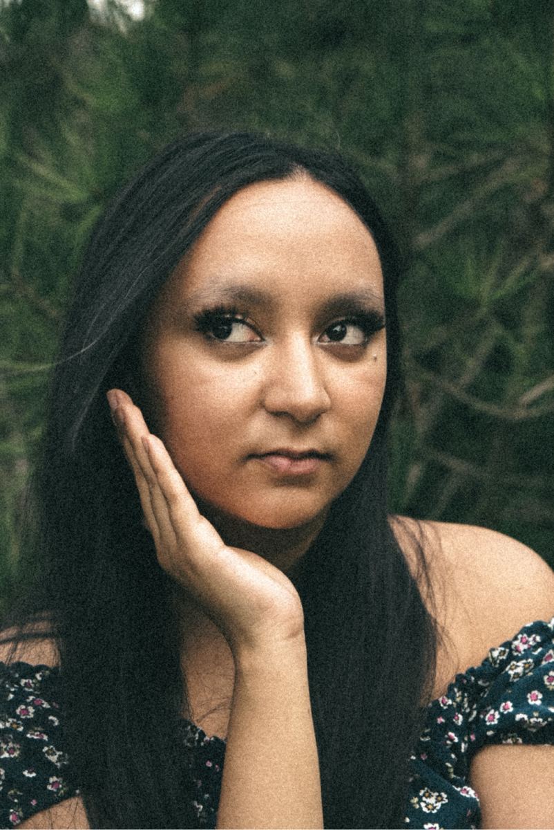 Portrait of a young woman resting her cheek on her hand against green foliage in Raleigh