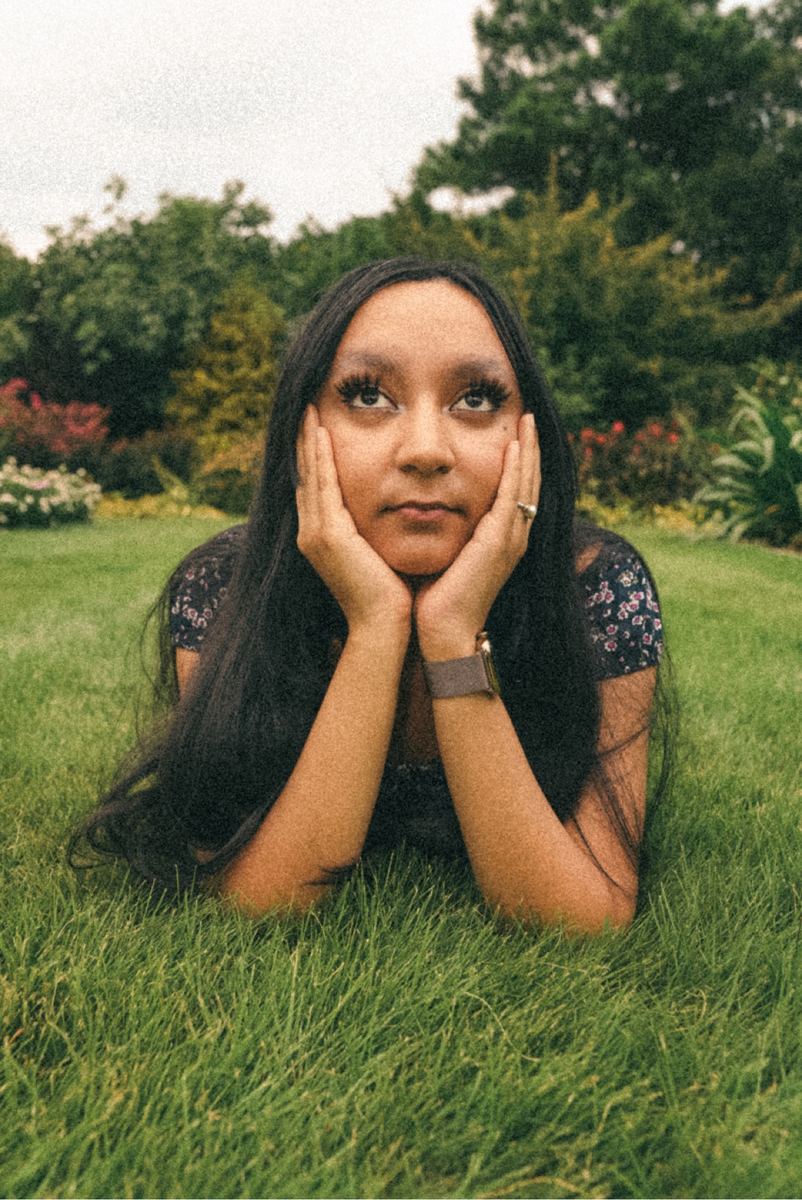 Playful portrait of a young woman lying on green grass with her chin in her hands