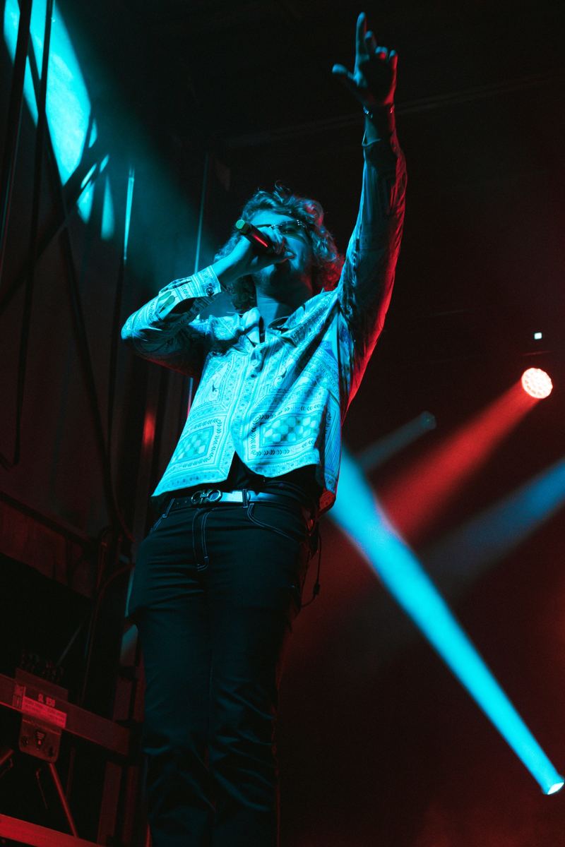 Performer singing into a microphone under blue and red stage lights in Raleigh