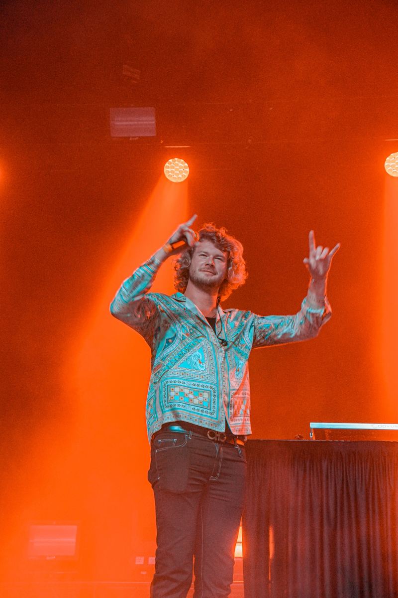 Musician with arms raised performing under warm orange stage lighting
