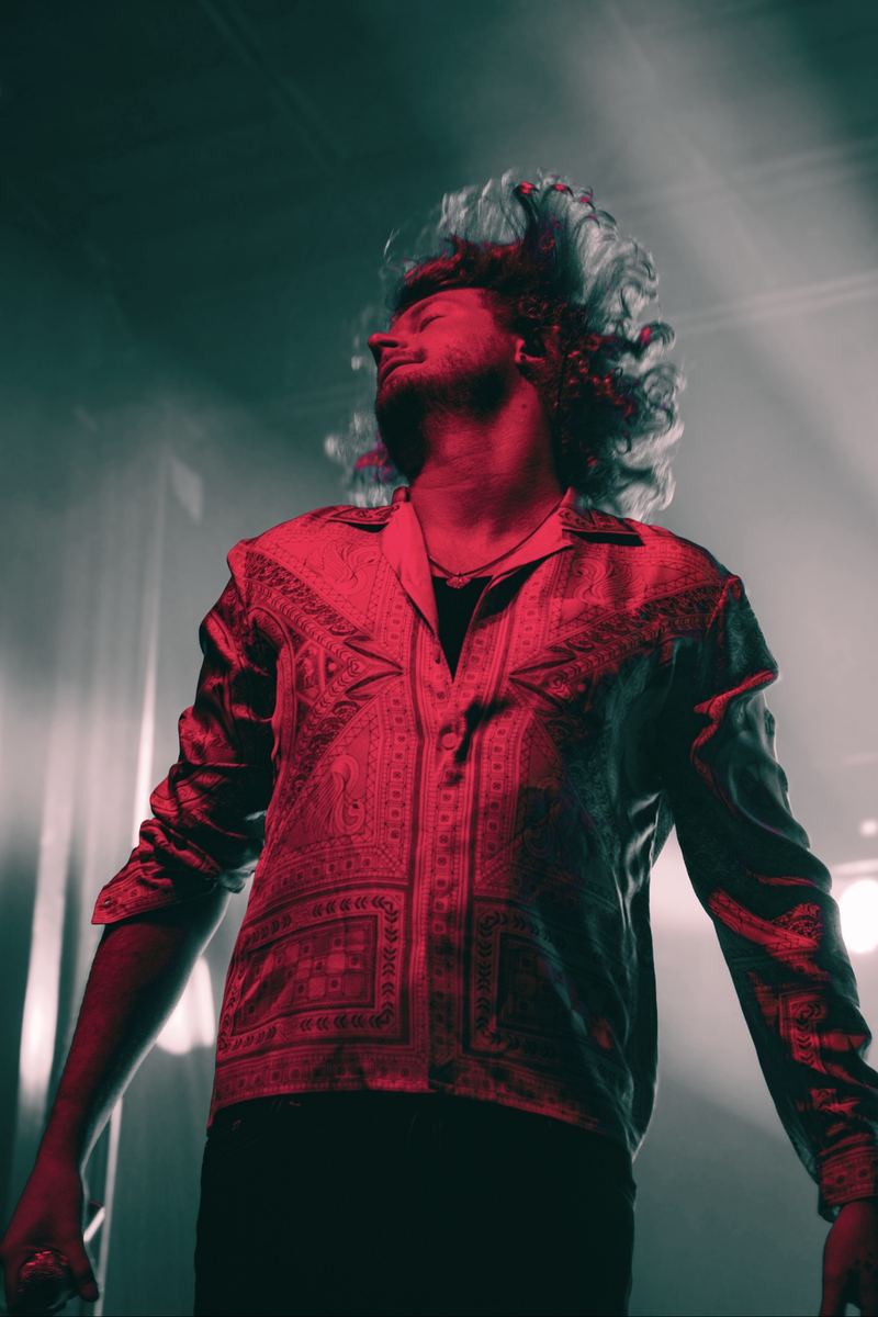 Performer looking skyward under red and green stage lights at a live concert