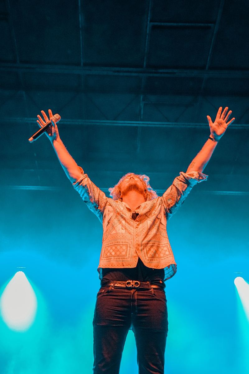 Musician with arms outstretched on stage under blue lights in Raleigh