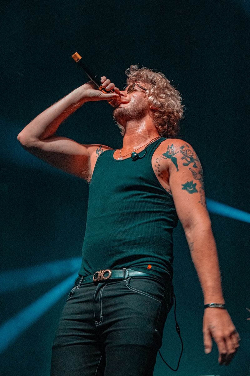Tattooed performer singing into a microphone on a dark stage in Raleigh